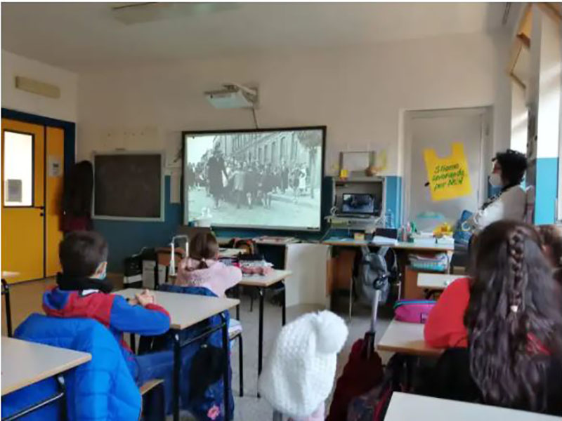 Bambini di spalle seduti in aula mentre guardano un film in bianco e nero
